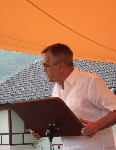 Buchautor Manfred Fock im weißen Kurzarmhemd liest konzentriert an einem hölzernen Notenständer.