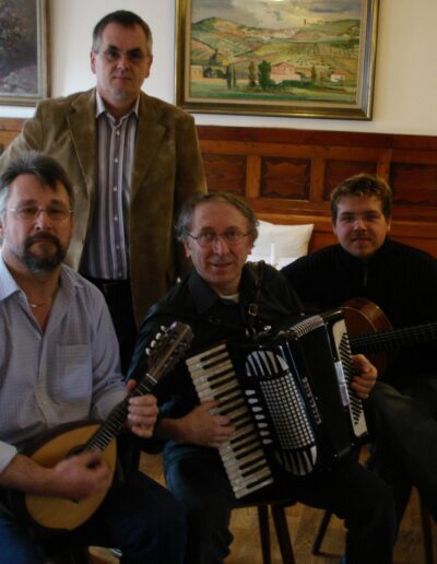 Buchautor Manfred Fock im beigen Sakko stehend hinter drei Musikern mit Mandoline, Akkordeon und Gitarre.