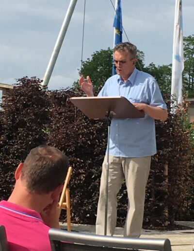 Buchautor Manfred Fock im hellblauen Hemd gestikuliert bei einer Open-Air-Lesung an einem Stehpult.