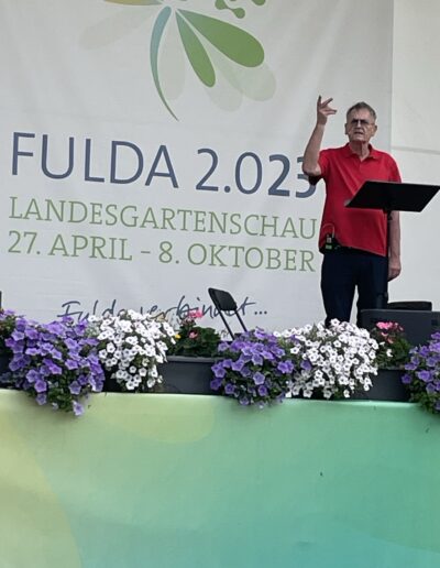 Buchautor Manfred Fock im roten Poloshirt hält eine Lesung auf der Bühne der Landesgartenschau Fulda.
