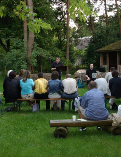 Buchautor Manfred Fock hält eine literarische Live-Lesung vor sitzendem Publikum in einem großen Garten.