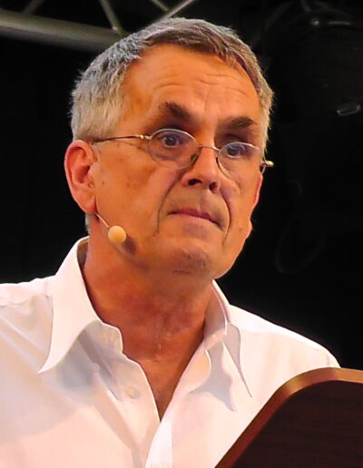 Porträt von Buchautor Manfred Fock im weißen Hemd während einer fokussierten Bühnenlesung.